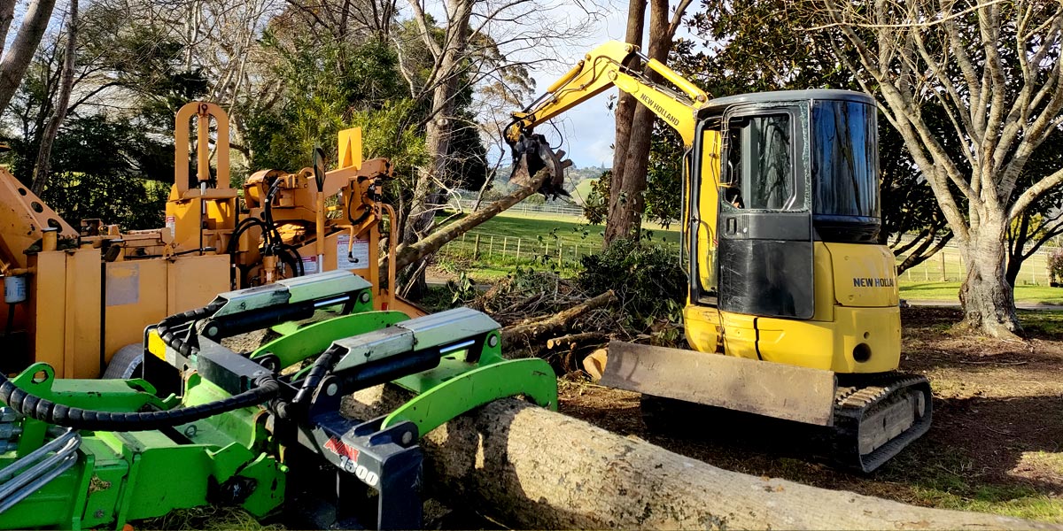Image showing a Jessep Contracting worker using machinery to pick up tree branches into a mulcher, while working on a site clearing job.