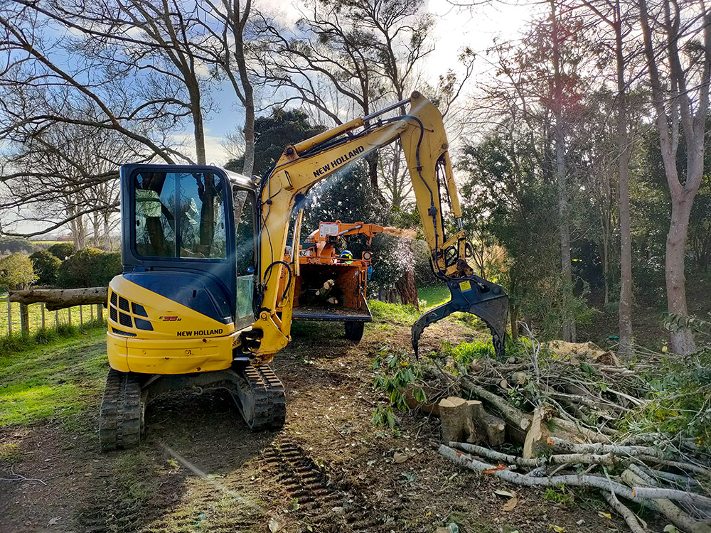 Image showing a Jessep Contracting worker using machinery to pick up tree branches into a mulcher, while working on a site clearing job.